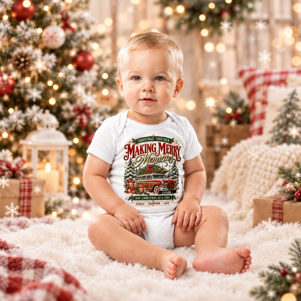 A baby sitting on a light gray studio background wearing a white short-sleeve bodysuit with a large vintage-style Christmas graphic on the front. The graphic includes red berries, green foliage, a blue sky, and decorative text reading 'The Magic Starts Here' and 'Togetherness'.