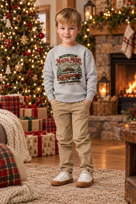 A young boy wearing a light gray crewneck sweatshirt with a vintage Christmas graphic, khaki pants, and white sneakers, standing against a plain white background.