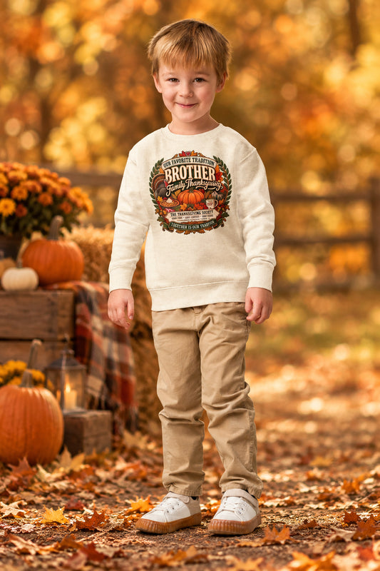 A young boy wearing a cream-colored crewneck sweatshirt with a colorful 'Brother' graphic on the chest, paired with khaki pants and white sneakers, standing against a plain white background.