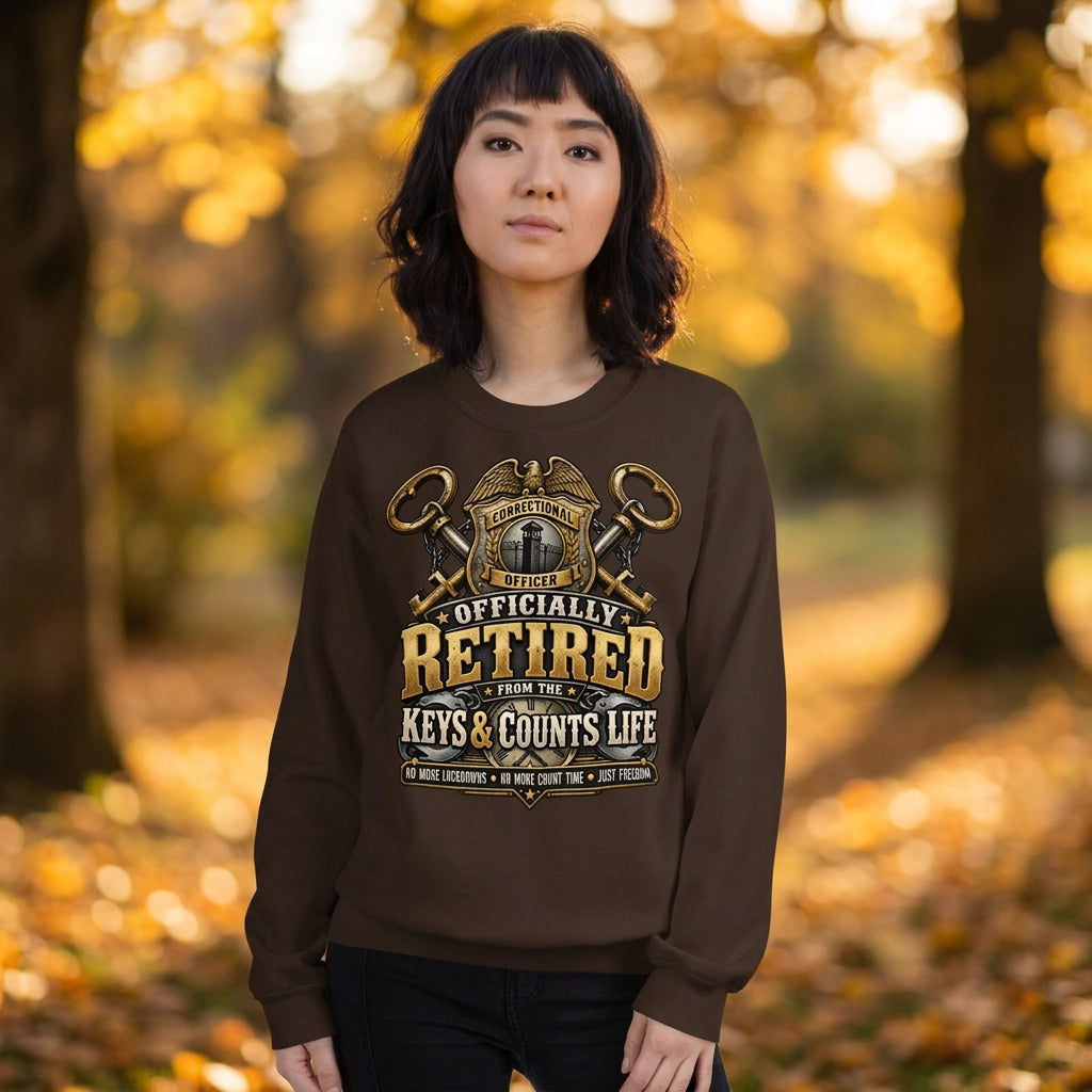 A woman wearing a dark brown crewneck sweatshirt with a gold and white graphic that reads 'OFFICIALLY RETIRED FROM THE KEYS & COUNTS LIFE'. The background is solid white.