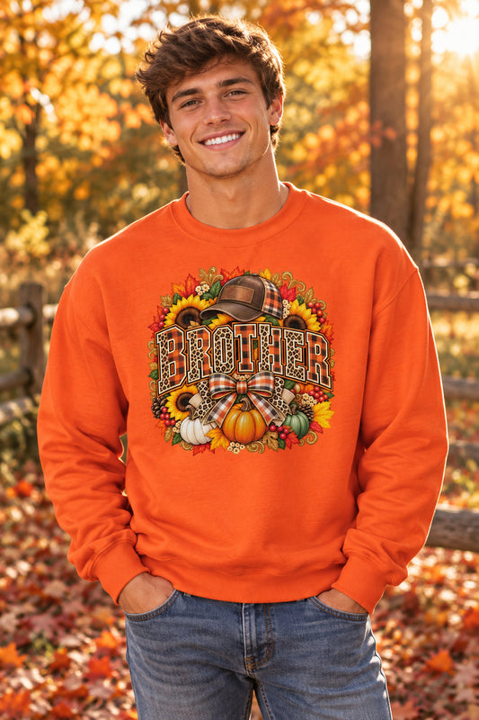 An orange crewneck sweatshirt featuring a large, colorful autumn-themed graphic on the front with the word 'BROTHER' in leopard-print letters, surrounded by pumpkins, sunflowers, and a plaid hat.
