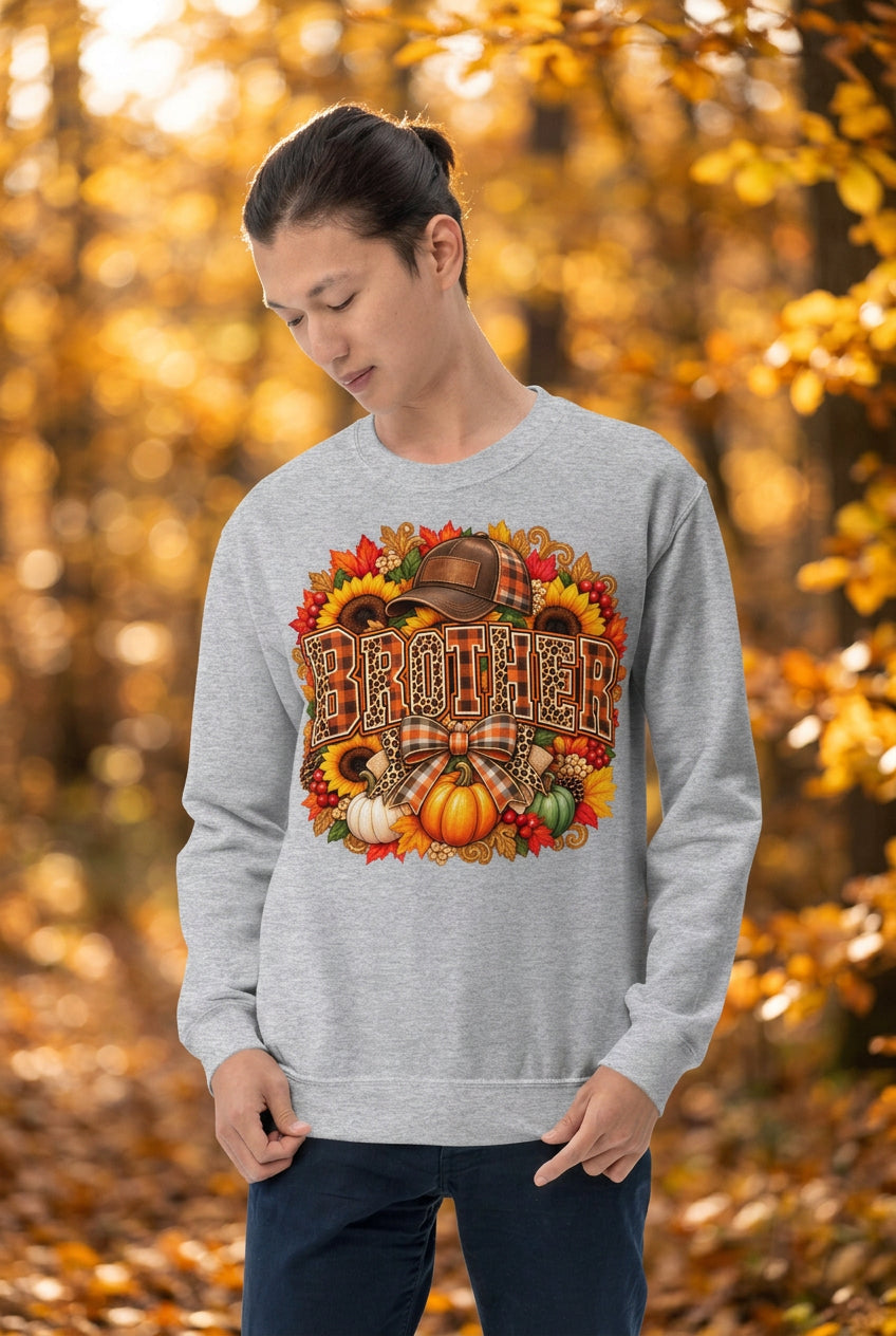 A man wearing a light heather gray crewneck sweatshirt with a large, colorful autumn-themed graphic on the chest that reads 'BROTHER' in plaid letters surrounded by pumpkins, sunflowers, and leaves.
