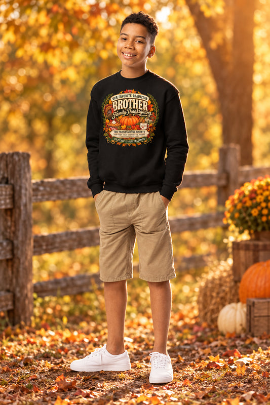 A young boy modeling a black crewneck sweatshirt with a colorful 'This is my Brother' Thanksgiving graphic, paired with khaki shorts and white sneakers, set against a plain white background.